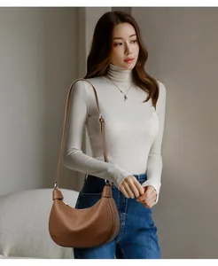 Detalle de un bolso de media luna en cuero marrón con patrón de lichi en una modelo con jersey