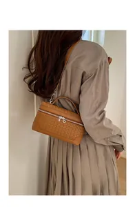Sac bandoulière marron tressé porté par un mannequin dans un décor d'intérieur épuré