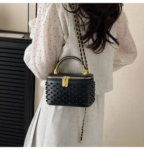 Close-up of black box bag with studs and golden chain worn on white dress