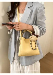 Detail of yellow lychee leather bucket bag featuring a plush bear and bead charm