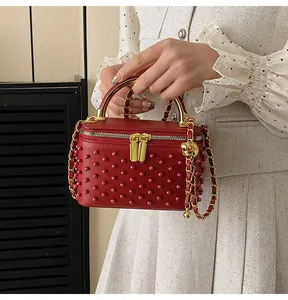 Close-up of a red leather mini box bag with beaded texture and gold metal handle
