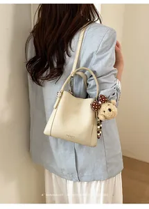 Detail of cream bucket bag in pebble leather with a cute plush bear charm hanging on side