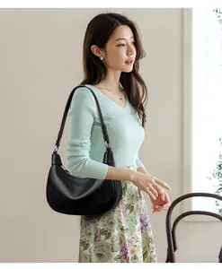 Detalle de bolso medialuna en cuero negro con textura de grano y correa ajustable
