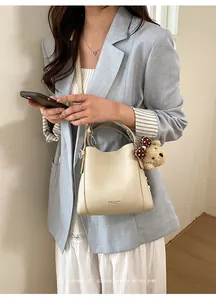 Detail of cream white leather bucket bag with teddy bear charm and logo print