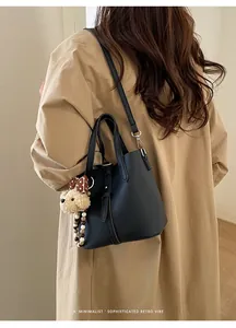 Detail of black lychee grain leather bucket bag with cute dog charm on trench coat