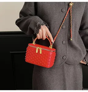 Detail of red crossbody box bag featuring tonal studs and a gold chain strap