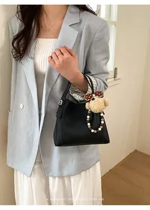 Detail of black retro bucket bag with lychee texture and cute plush bear charm decoration