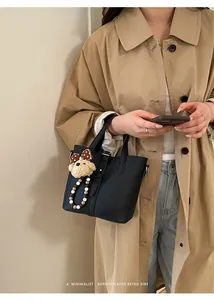Detail of black lychee grain bucket bag with cute plush dog pendant on beige trench coat