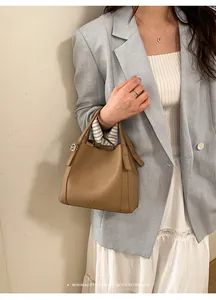 Close-up of brown lychee leather bucket bag held by model wearing a light blue suit