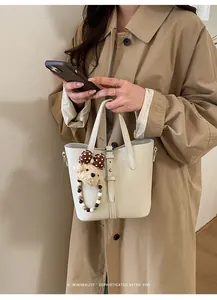 Detail of off-white lychee grain bucket bag featuring a cute teddy bear charm and metal D-ring