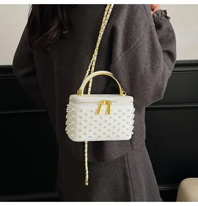 Detailed view of white pearl-embellished box bag with gold handle on elegant model