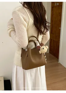 Detail of dark brown leather bucket bag with a plush bear charm on a model