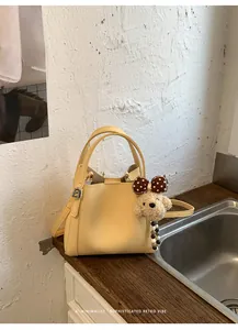 Detail of yellow pebbled leather bucket bag with cute plush puppy charm and silver hardware