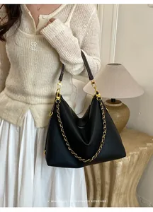 Detail of black pebbled leather tote with golden chain strap and zip closure on a model