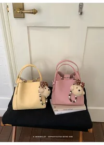 Close-up of litchi texture bucket bags in cream and pink with cute plush charms