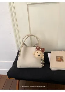 Detail of off-white lychee texture bucket bag with plush bear charm on black leather bench