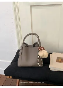 Detail of taupe leather bucket bag with brand embossing and cute plush puppy charm