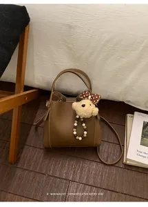 Close-up of dark brown lychee texture leather bucket bag with cute bear charm detail