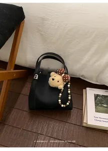Close-up of black lychee leather bucket bag with cute plush bear pendant and double handles