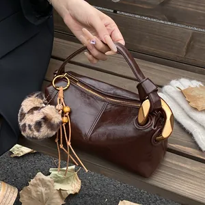 Detail of dark brown oil wax leather pillow bag with gold clasp and leopard fur pompom
