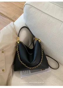 Detail of soft black lychee grain leather tote bag with gold chain and strap on beige sofa