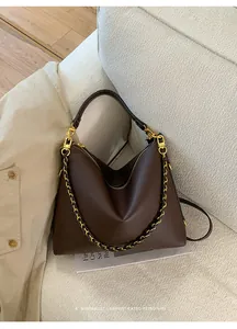 Macro shot of dark brown pebbled leather texture and golden chain strap on a tote bag