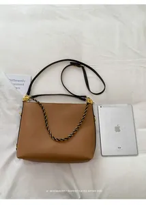 Detail view of caramel lychee grain leather tote bag with braided chain strap on white fabric