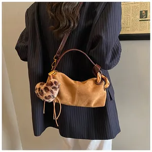 Brown suede pillow bag featuring gold chain details and leopard heart charm on a model