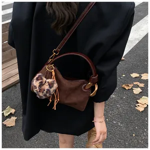 Detail of brown suede crossbody bag with gold metal handle and leopard heart charm