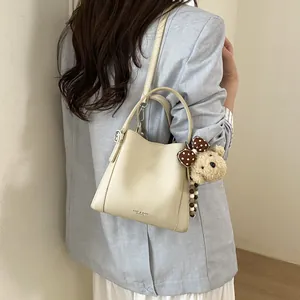 Off-white lychee leather bucket bag with top handle, shoulder strap and plush bear charm