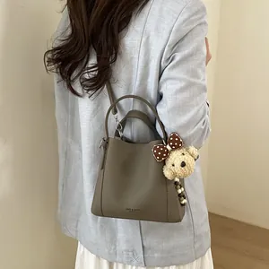 Brown leather bucket bag with litchi texture and cute teddy bear charm on shoulder strap