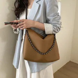 Brown soft leather hobo tote bag with gold chain strap worn by a model in casual blazer
