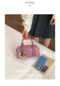 Pink leather Boston bag with wooden horse charm and double handles on a white background