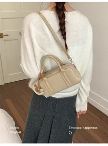 Beige Boston handbag shown on model featuring a wooden horse charm detail and strap