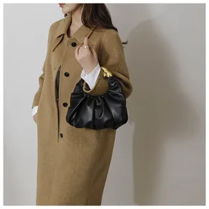 Black pleated cloud handbag with elegant gold curved metal handle on camel coat