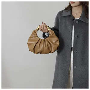 Detailed view of a brown pleated cloud bag with circular gold metal handle on a model