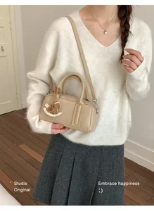 Detail of beige Boston bag with horse charm, worn by model in minimalist knit sweater