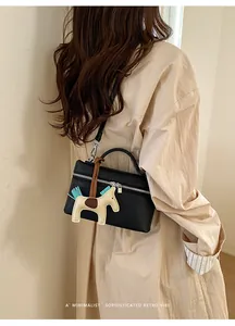 Détail du sac bandoulière en cuir noir avec breloque cheval beige et finitions argentées