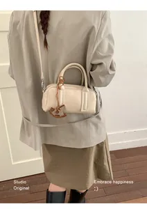 Close-up of cream Boston bag with leather texture and horse charm on a grey blazer outfit