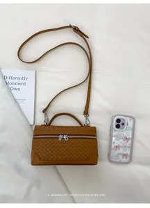 Sac à main marron tressé avec poignée et bandoulière à côté d'un téléphone portable