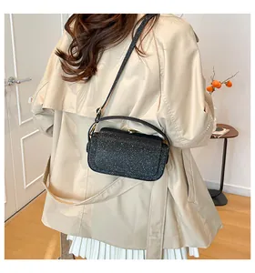 Vue détaillée du sac bandoulière noir pailleté avec fermoir doré sur manteau beige