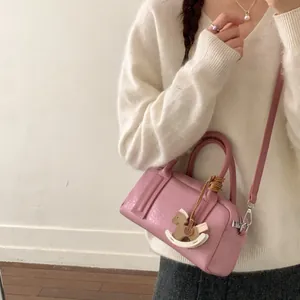 Pink lychee textured leather Boston bag with horse charm held by model in casual style