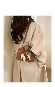 Sac boîte en cuir marron avec fermeture éclair argentée et breloque cheval sur modèle