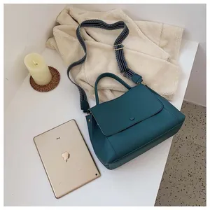 Teal leather handbag with striped strap shown next to an iPad for size reference