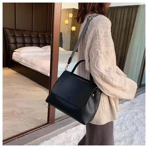 Close-up of black leather handbag featuring a geometric patterned wide woven strap
