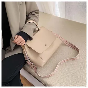 Detail of minimalist beige handbag with decorative round metal clasp and woven strap
