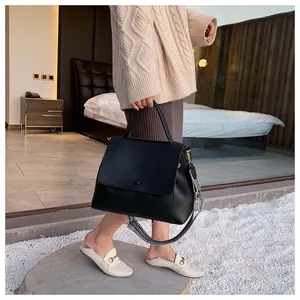Detail of black top handle bag with geometric wide strap and gold hardware accents