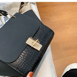Close-up of golden metal lock and crocodile texture on black crossbody bag