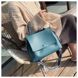 Detail of teal leather handbag showing matte texture and woven striped shoulder strap