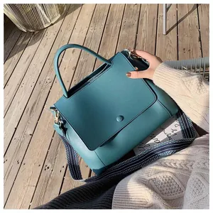 Close-up of teal textured leather handbag with a striped fabric strap on wooden floor